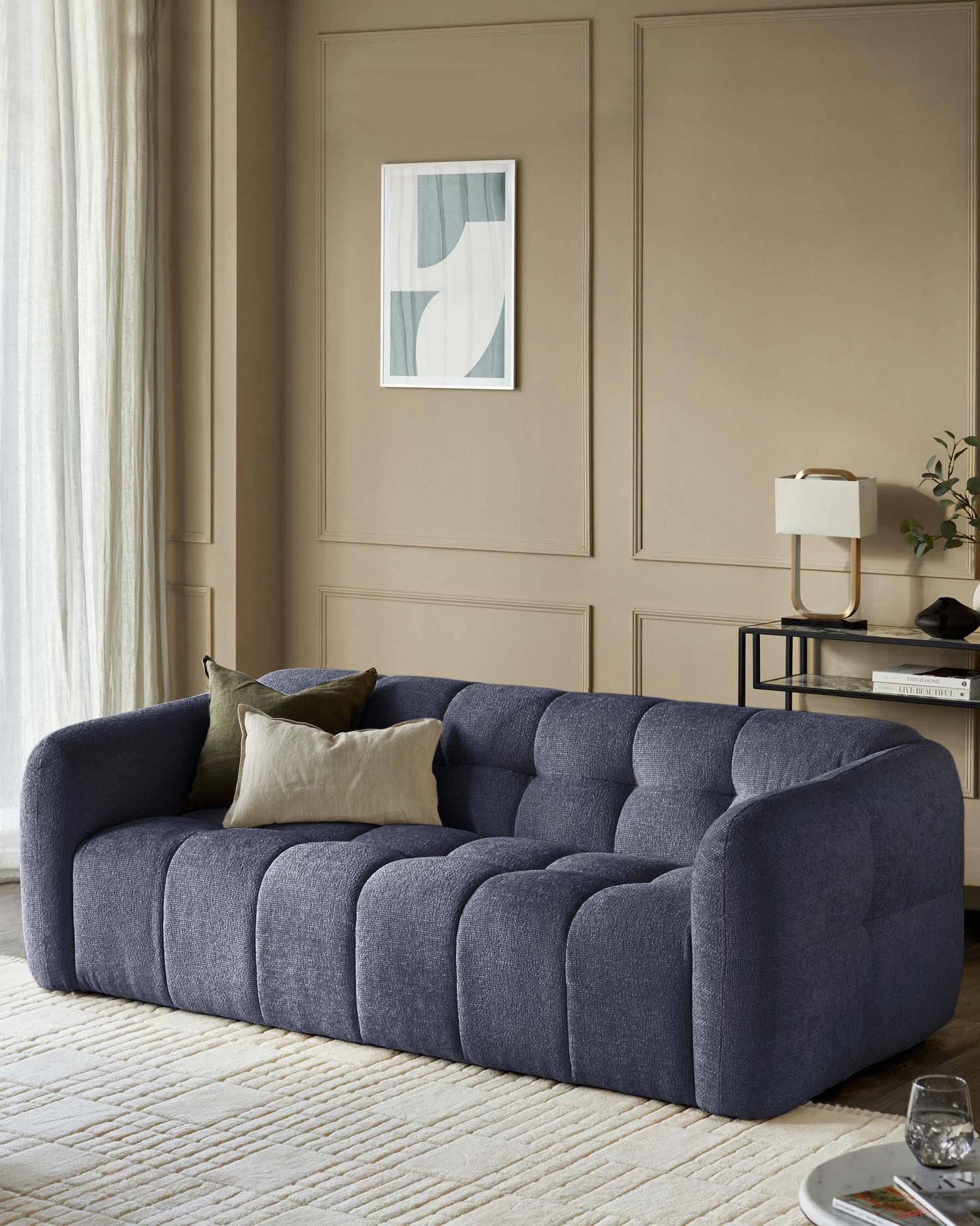 A blue, tufted sofa with a curved design sits in a living room with neutral decor and cushions.