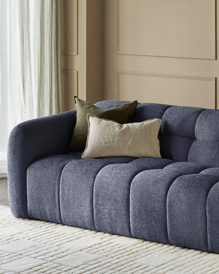 Hayes 3-seater sofa in dark blue weave fabric with channel quilting, styled with neutral pillows in a bright room.