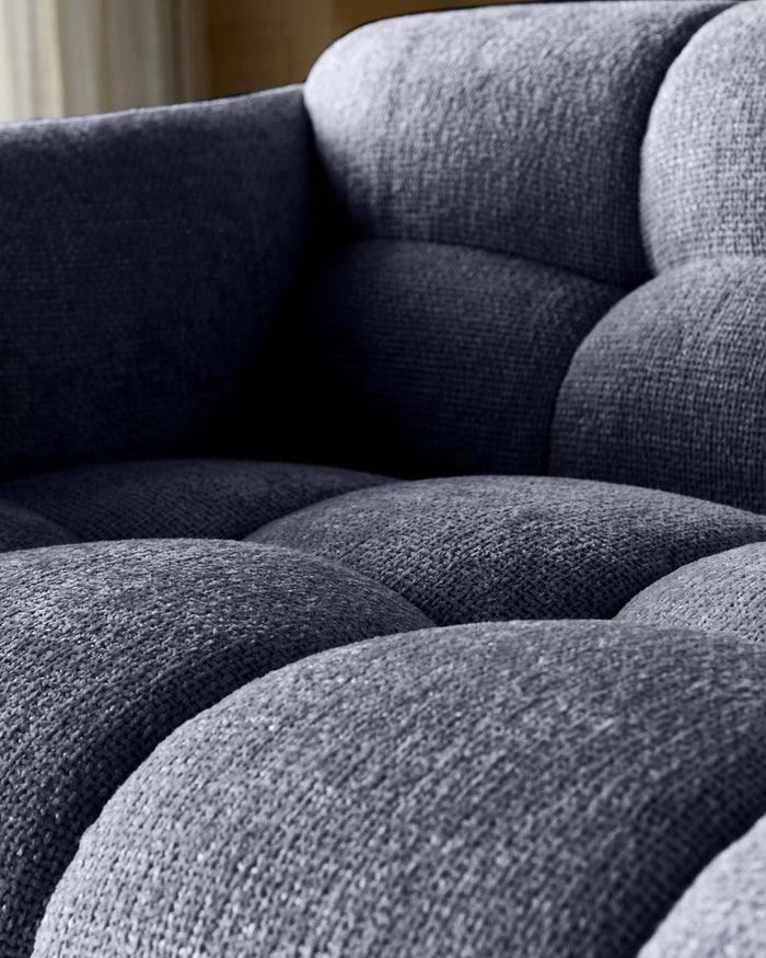 Close-up of a stylish, modern grey fabric sofa with a textured, pillowed design. Comfortable and inviting furniture.