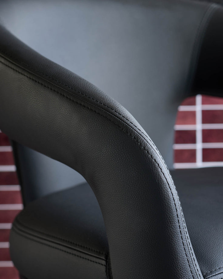 Close-up of a black leather chair with detailed stitching, showcasing its design and material quality.