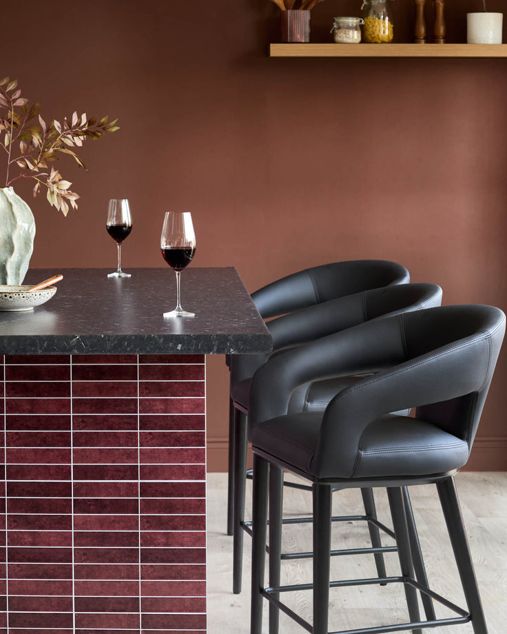 Close up of three bar stools positioned at a kitchen counter with two wine glasses sat on top of it.