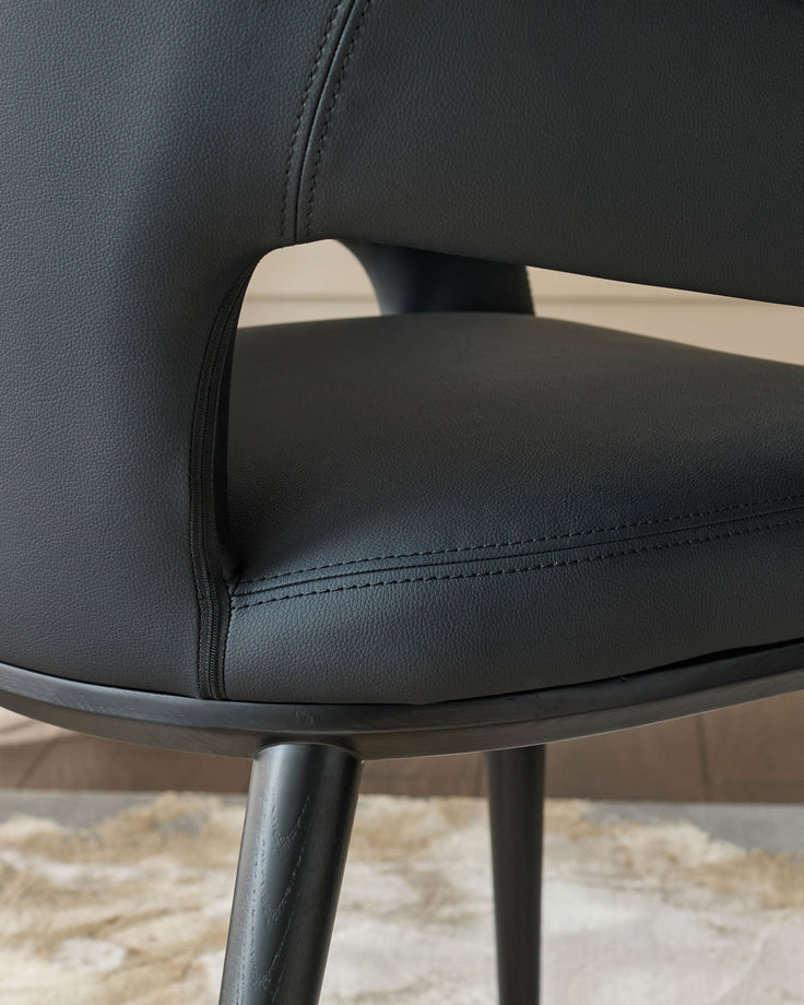 Close-up of a black leather chair with stitching detail, showcasing its design and craftsmanship.