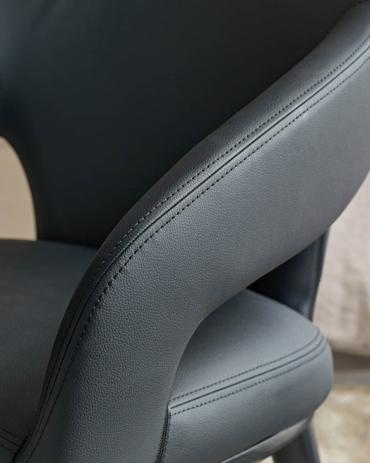 A close up of a black faux leather chair with stylish stitching detail.