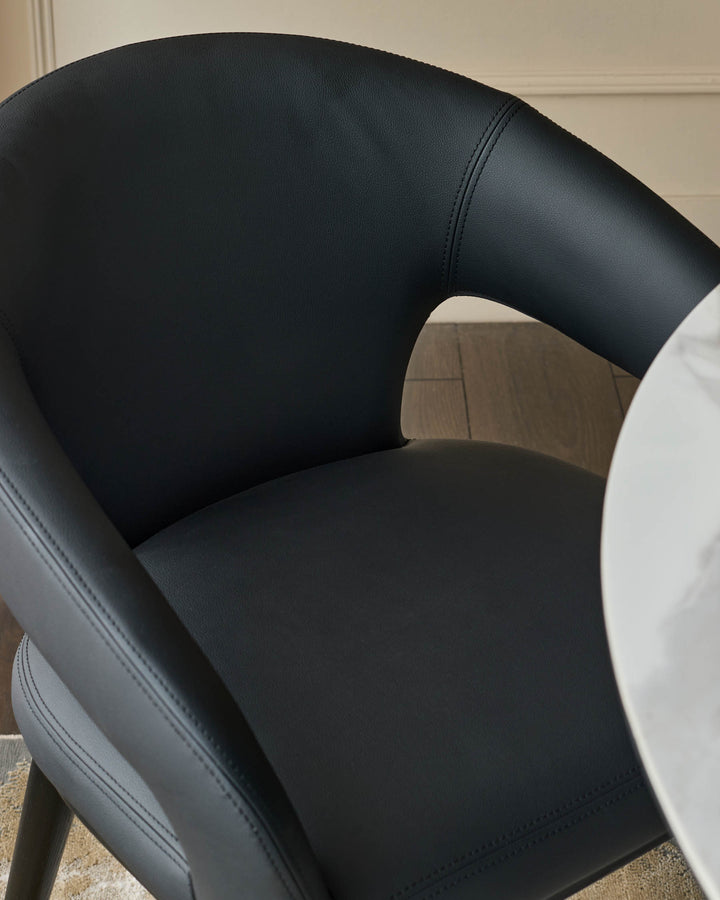 A sleek black leather chair curves elegantly around a small round table with a marble effect top.