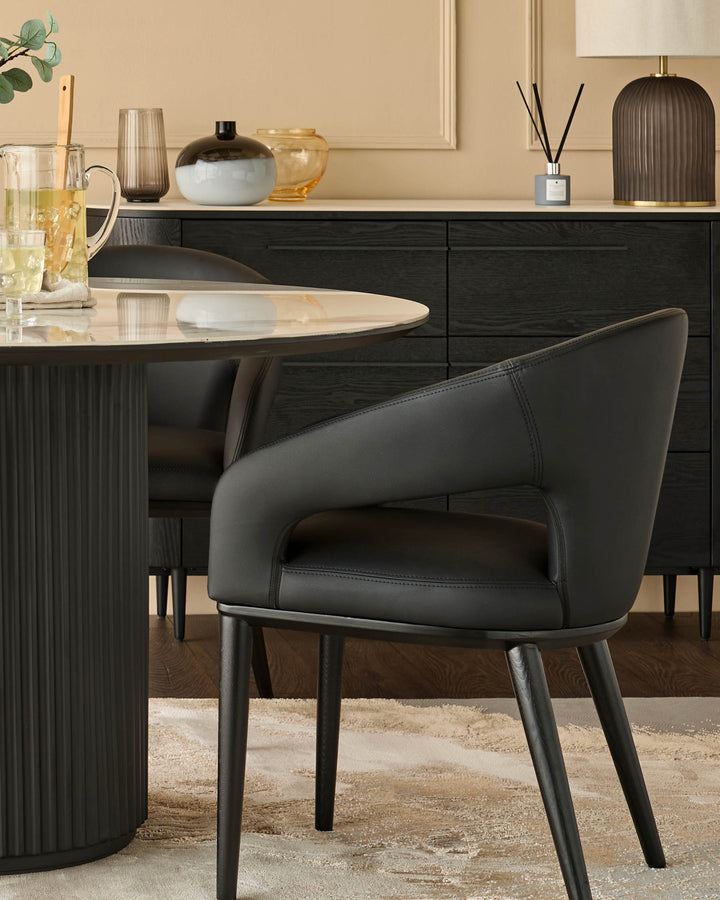A modern dining set featuring a round marble table with a black pedestal base and black leather chairs.