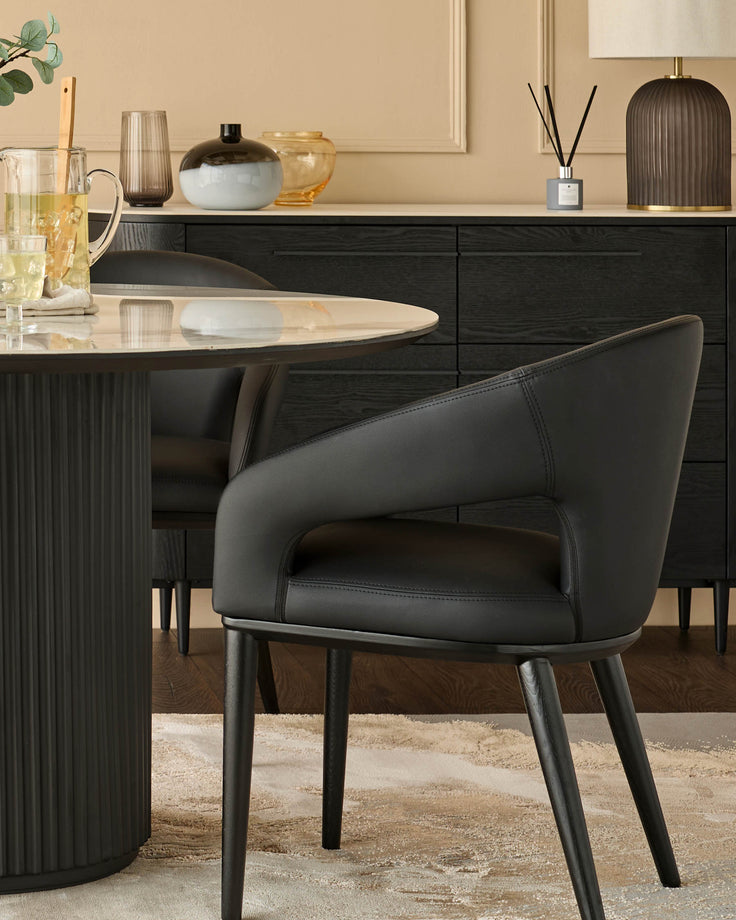 A modern dining set featuring a round marble table with a black pedestal base and black leather chairs.