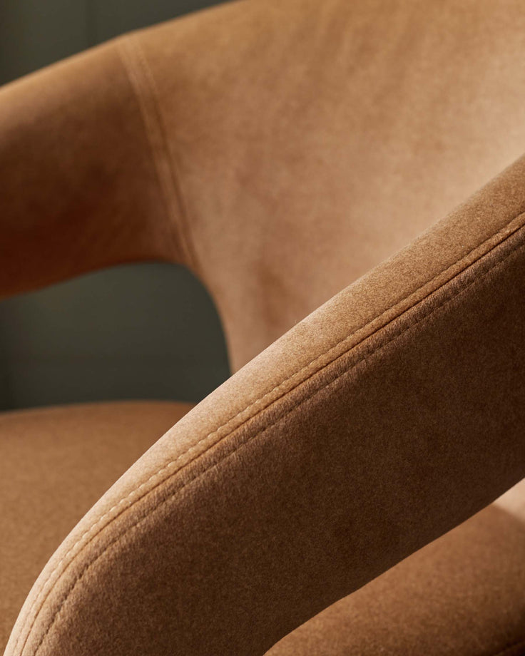 Close-up of a stylish armchair with a textured, brown upholstery, showcasing the curved armrest and stitched detailing.