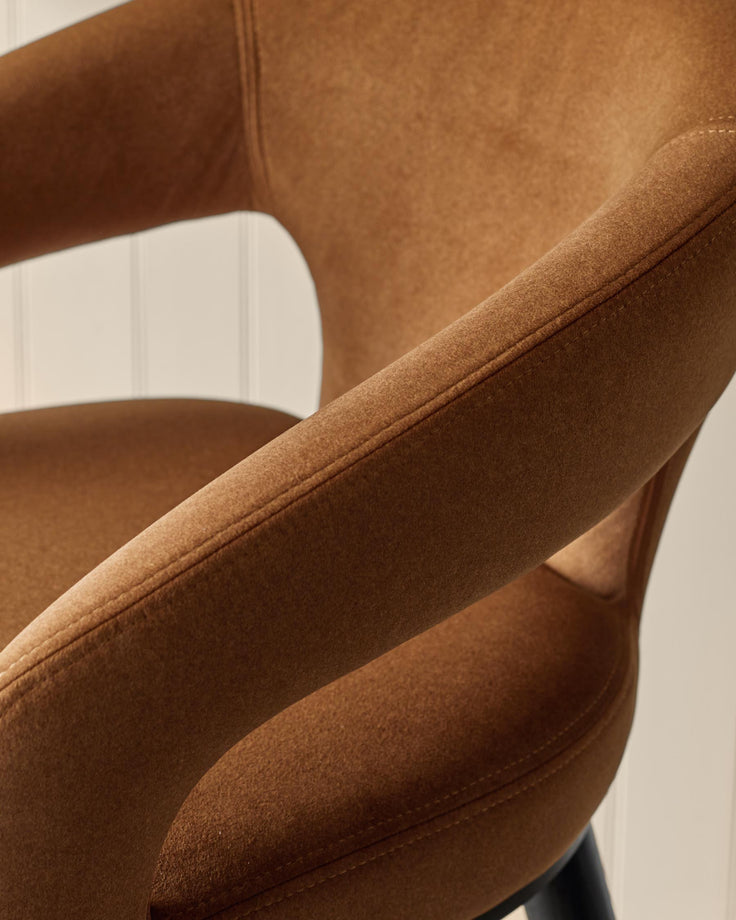 Close-up of a brown upholstered chair with a curved armrest, showcasing its texture and design, for a furniture website.