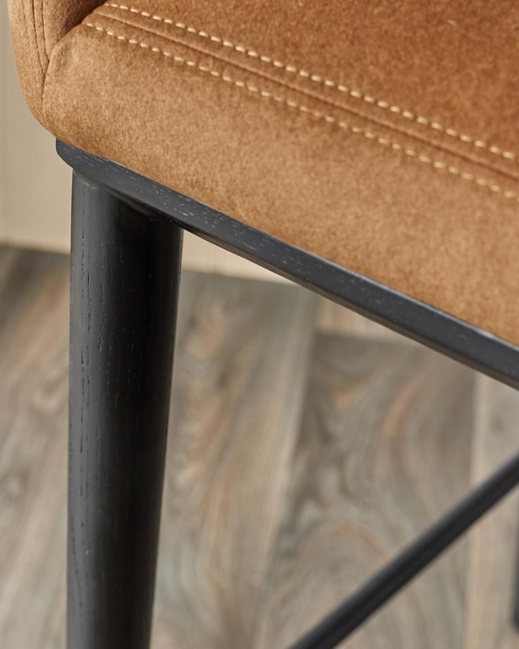 Close-up of a stool featuring a brown, padded seat with stitching, and dark wooden legs.