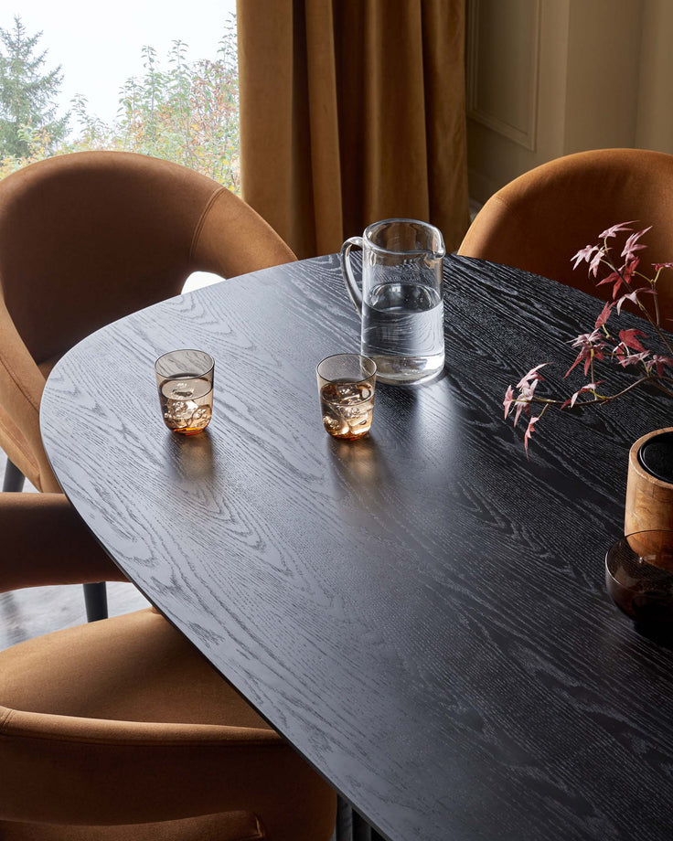 Stylish dining area with a black wood table, amber chairs, and window with mustard curtains.