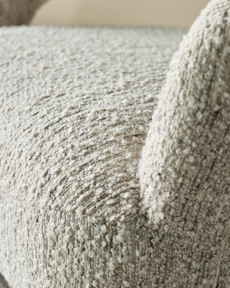 Close-up of a textured, light grey upholstered armchair, showing the detailed fabric and armrest.