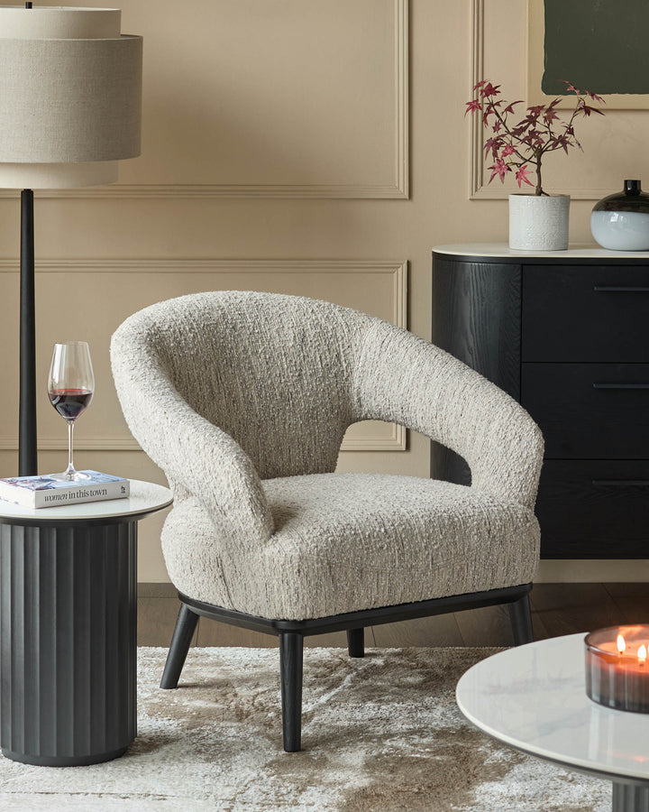 An armchair, dark wood chest of drawers and a lamp, complemented by round side tables and a patterned rug.