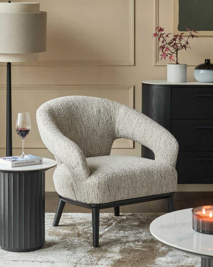 An armchair, dark wood chest of drawers and a lamp, complemented by round side tables and a patterned rug.