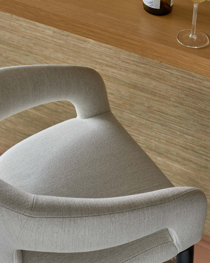 Stylish curved grey upholstered chair with a sleek design, complemented by a warm wooden bar top and glassware in the background.