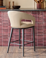 A stylish, light beige bar stool with black legs sits against a red tiled splashback in a modern kitchen setting.