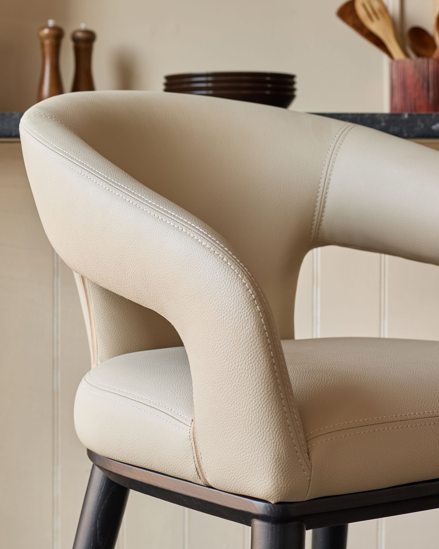 An upholstered, cream coloured bar stool with black legs in a domestic kitchen setting.