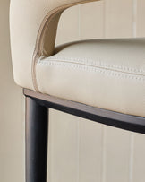 Close-up of a stylish chair with cream leather upholstery and dark wooden legs against a neutral panelled backdrop.