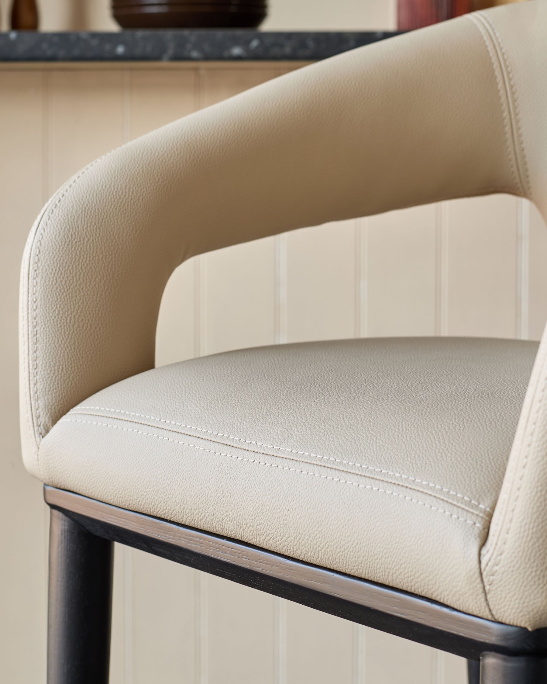 Beige bar stool with curved arms and dark wood frame. Modern design for kitchen islands and home bars.