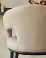 Close-up of a stylish, cream-coloured bar stool with a curved backrest and black wooden legs.