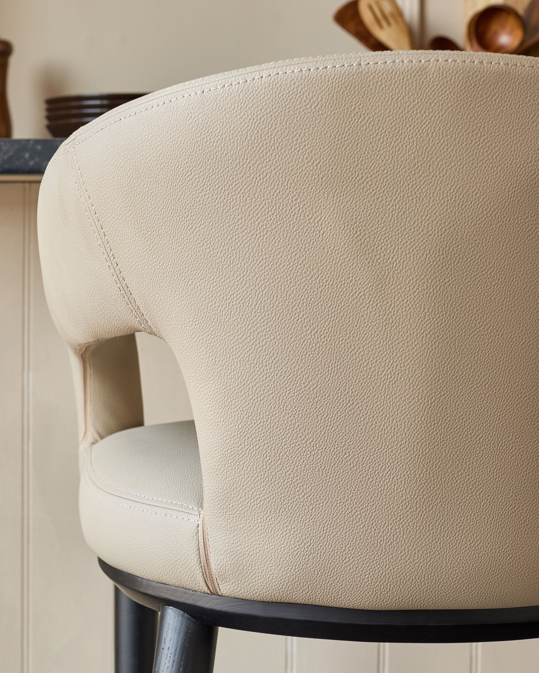 Close-up of a stylish, cream-coloured bar stool with a curved backrest and black wooden legs.