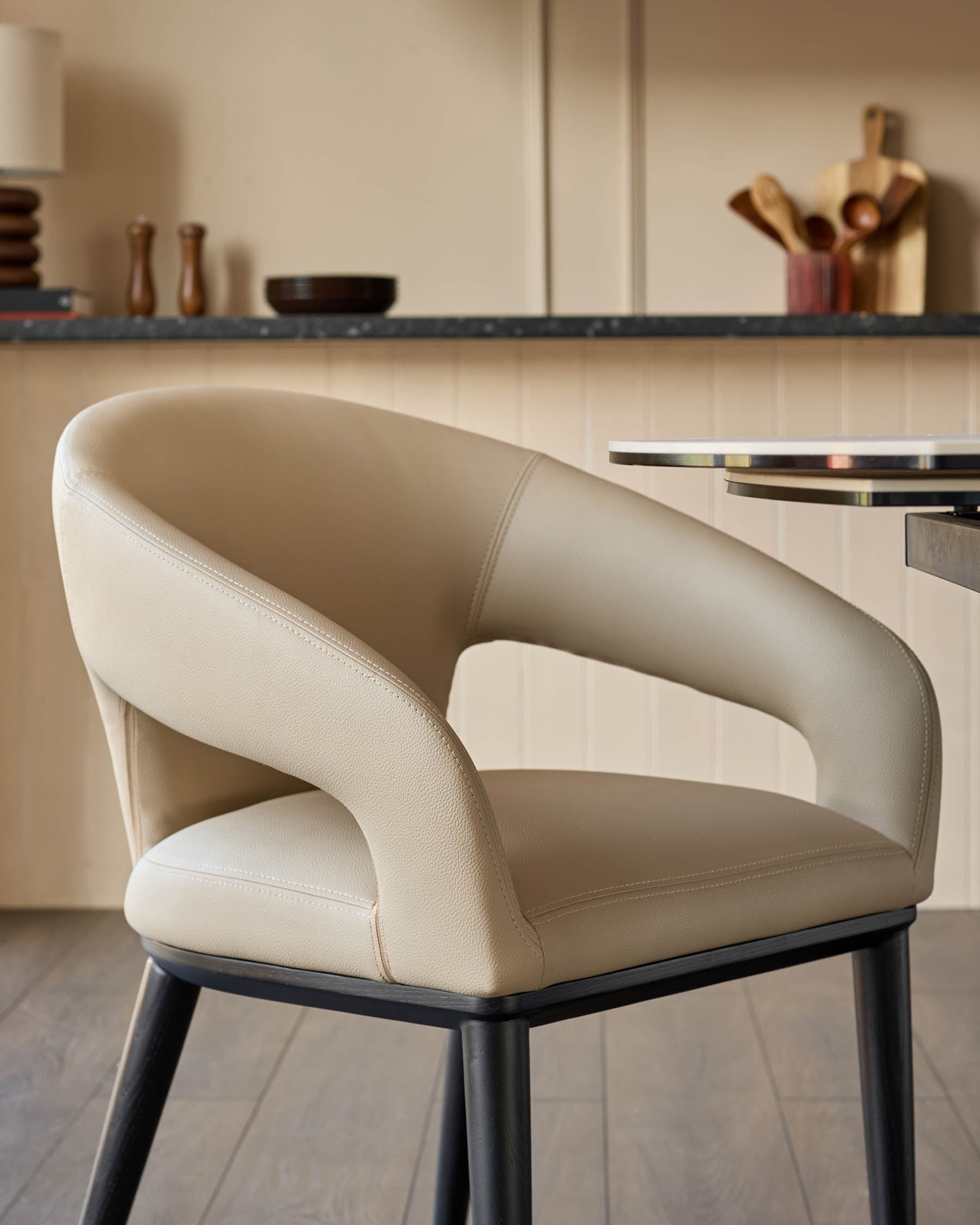 A modern, armless beige leather chair with dark wood legs is featured in a kitchen setting.