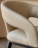 Close-up of a modern armchair with beige upholstery and black legs, showcasing its sleek design.