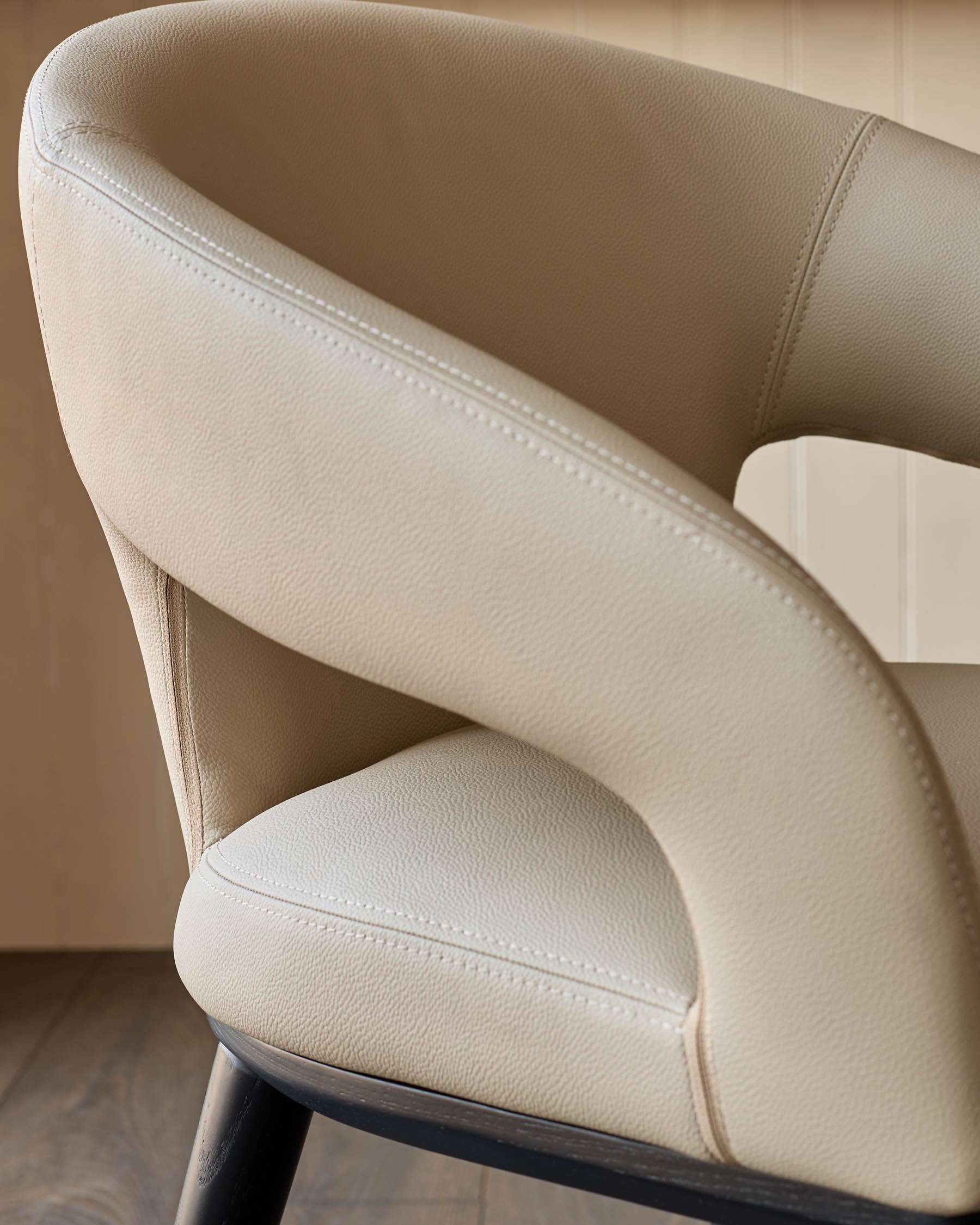 Close-up of a modern armchair with beige upholstery and black legs, showcasing its sleek design.
