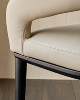 Close-up of a chair with cream leather upholstery and a dark wood frame, showcasing modern design and luxurious comfort.