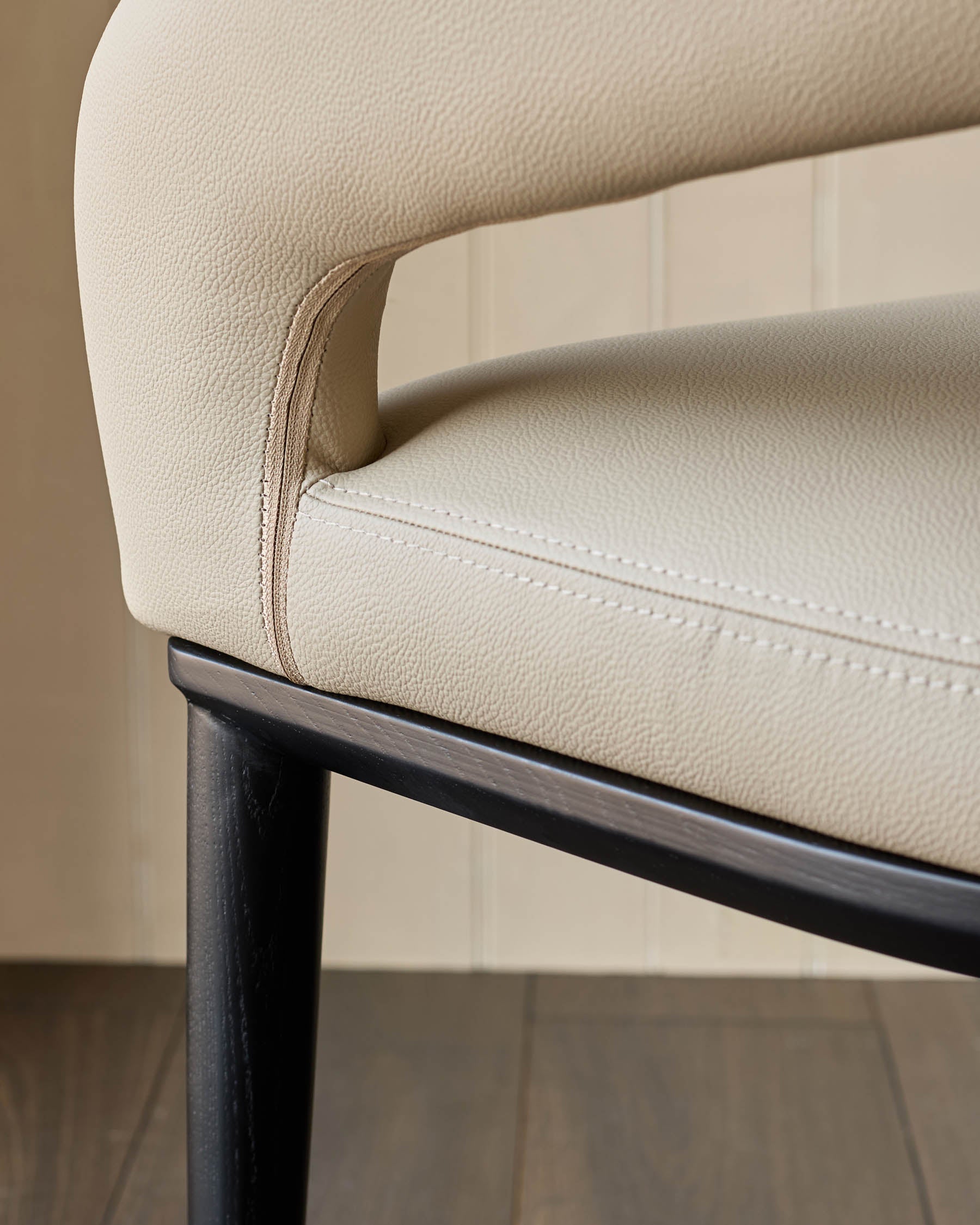 Close-up of a chair with cream leather upholstery and a dark wood frame, showcasing modern design and luxurious comfort.