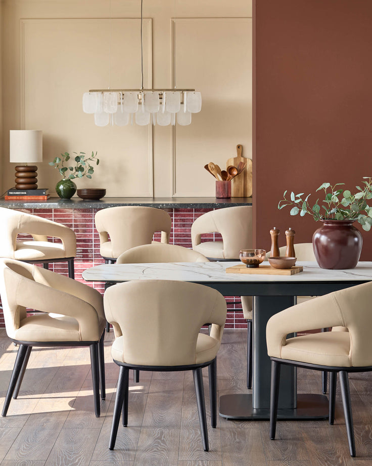 A modern dining set features beige upholstered chairs with black legs around a white marble-effect table, lit by a stylish chandelier.