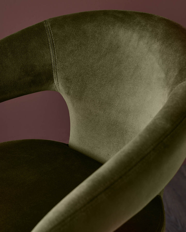 Close-up of a stylish, modern olive green velvet chair with a curved back and seat. Minimalist design.