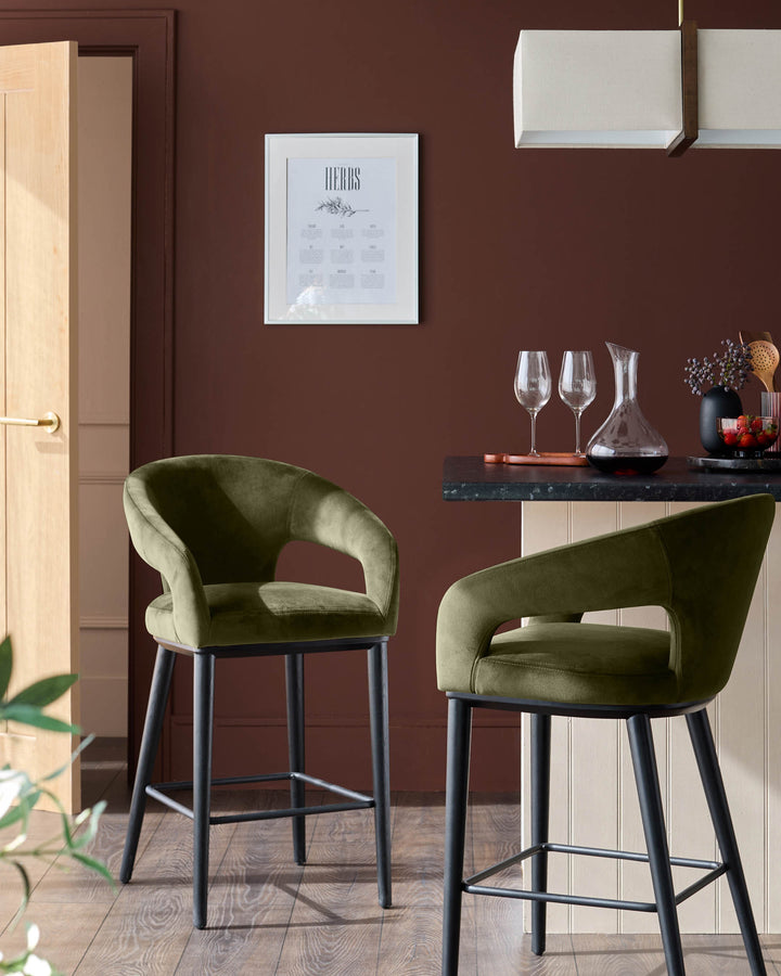 Two stylish green velvet bar stools with black legs sit at a kitchen counter in a warm, modern interior.