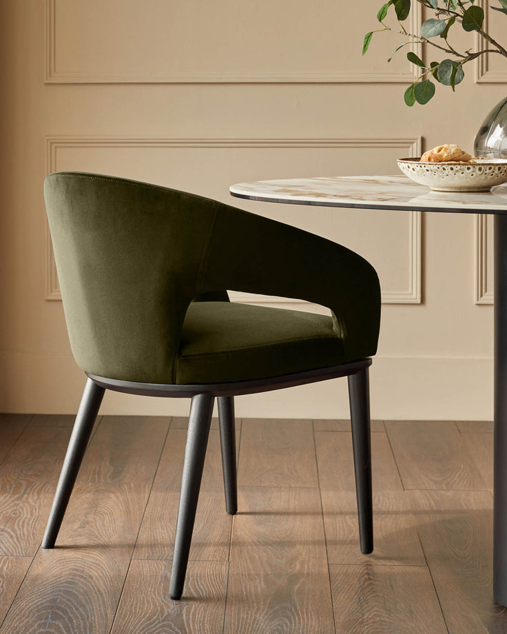Green velvet chair with armrests positioned next to a round table with a marble-effect top in a stylish interior.