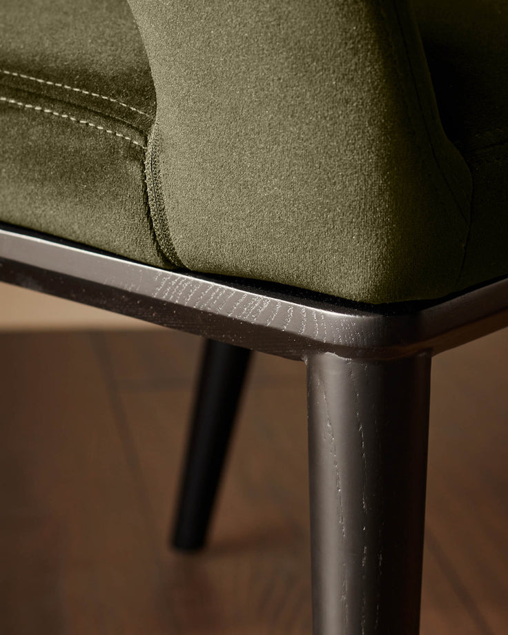 Close-up of an olive green upholstered armchair with dark wood legs and frame. Modern design meets comfort.