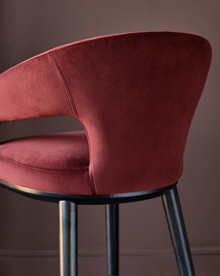 Close-up of a stylish red velvet bar stool with black legs against a brown backdrop. Modern furniture design.