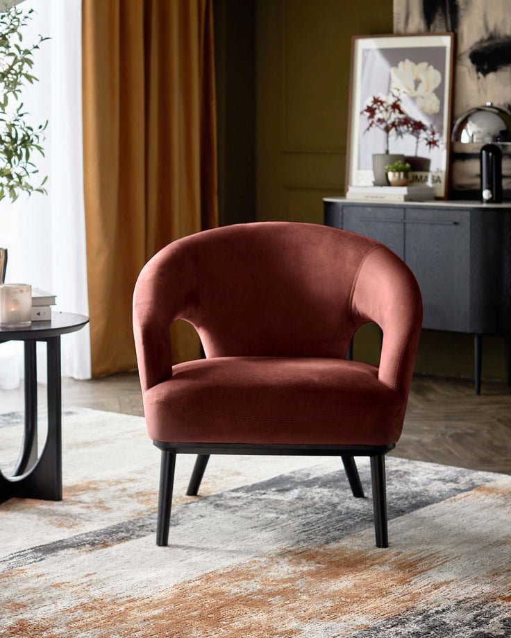 A plush, brick-red velvet armchair with a sleek black frame adds a touch of luxury to this interior setting.