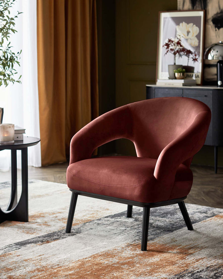 A plush red armchair with black legs sits on a patterned rug, beside a black side table. Stylish and modern.