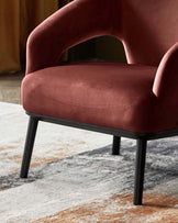 Heath accent chair in toffee red velvet with curved arms and black legs, side view on patterned rug.