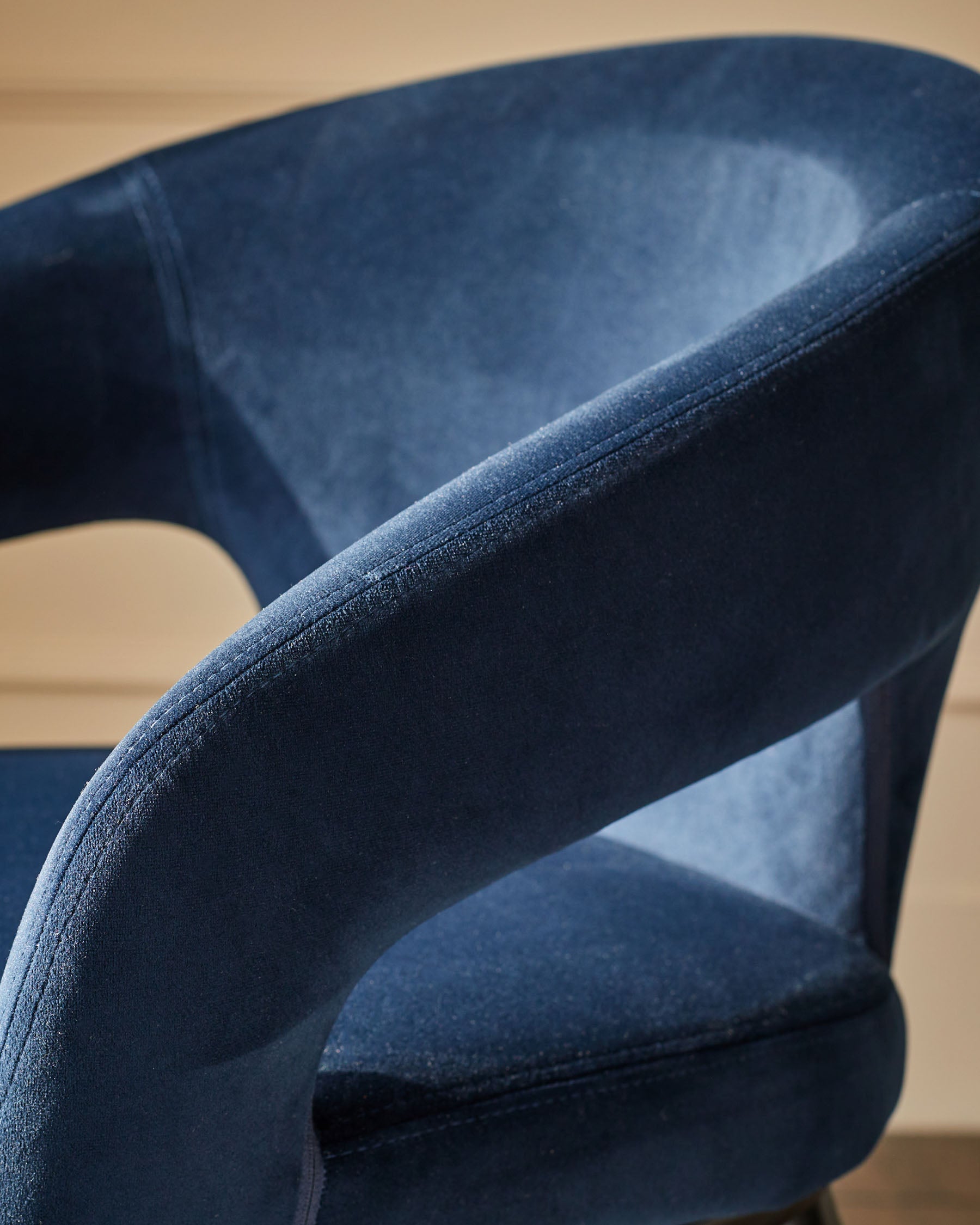 Close-up of a blue, cushioned chair with a curved back and armrest, exuding comfort and style.