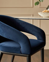 A navy velvet chair with sleek, modern lines is partially seen next to a round table with a bowl of bread.