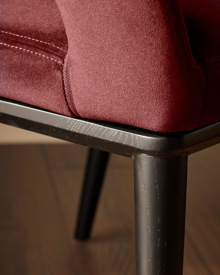 Close up of a burgundy chair with wooden legs. The fabric is textured with visible stitching details.