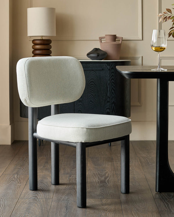 Henley dining chair in ivory fabric with blackwood finish, rounded back and seat, cylindrical legs, shown in styled room setting.