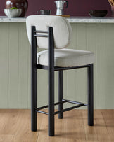 Henley bar stool with ivory fabric seat and back, black wood frame, footrest, shown in kitchen setting.