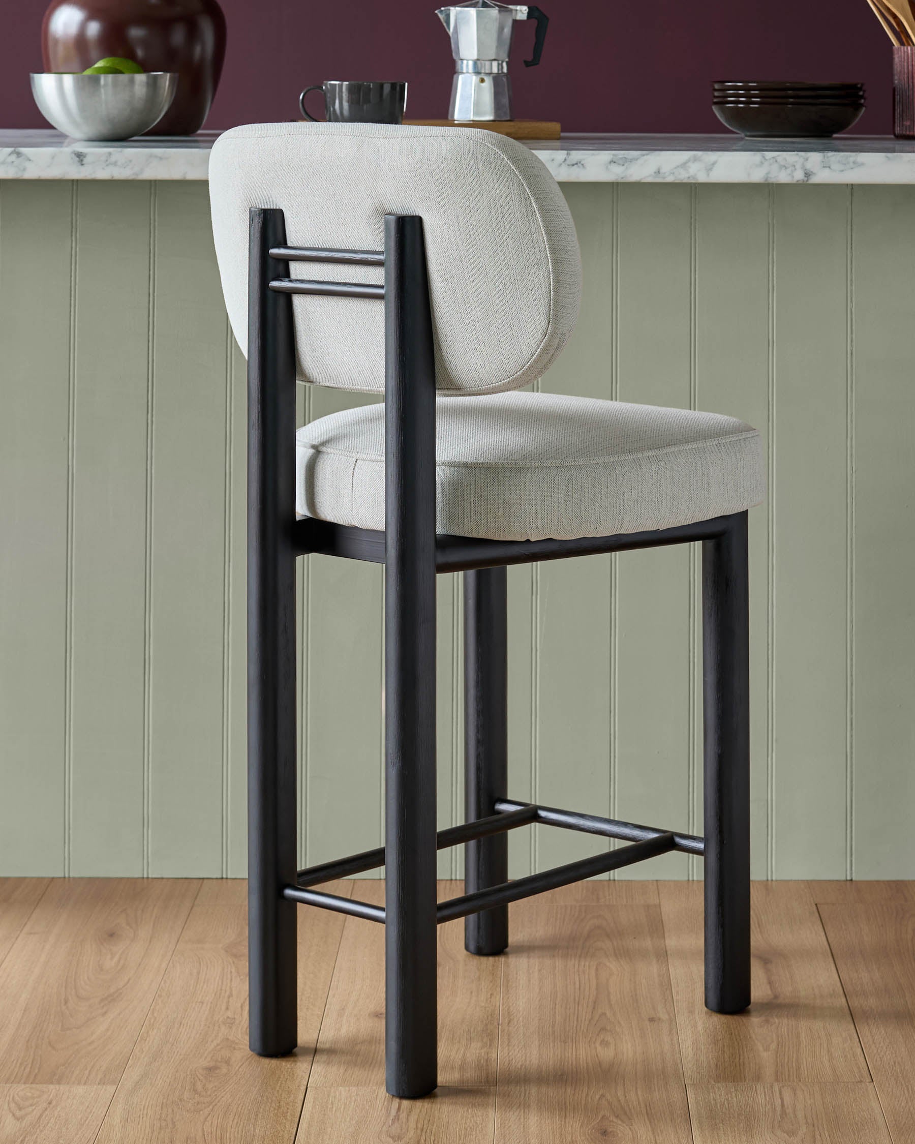 Henley bar stool with ivory fabric seat and back, black wood frame, footrest, shown in kitchen setting.
