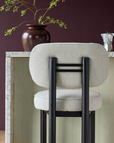 Henley bar stool in ivory fabric with black wooden frame, rounded backrest, and seat detail against marbled counter.