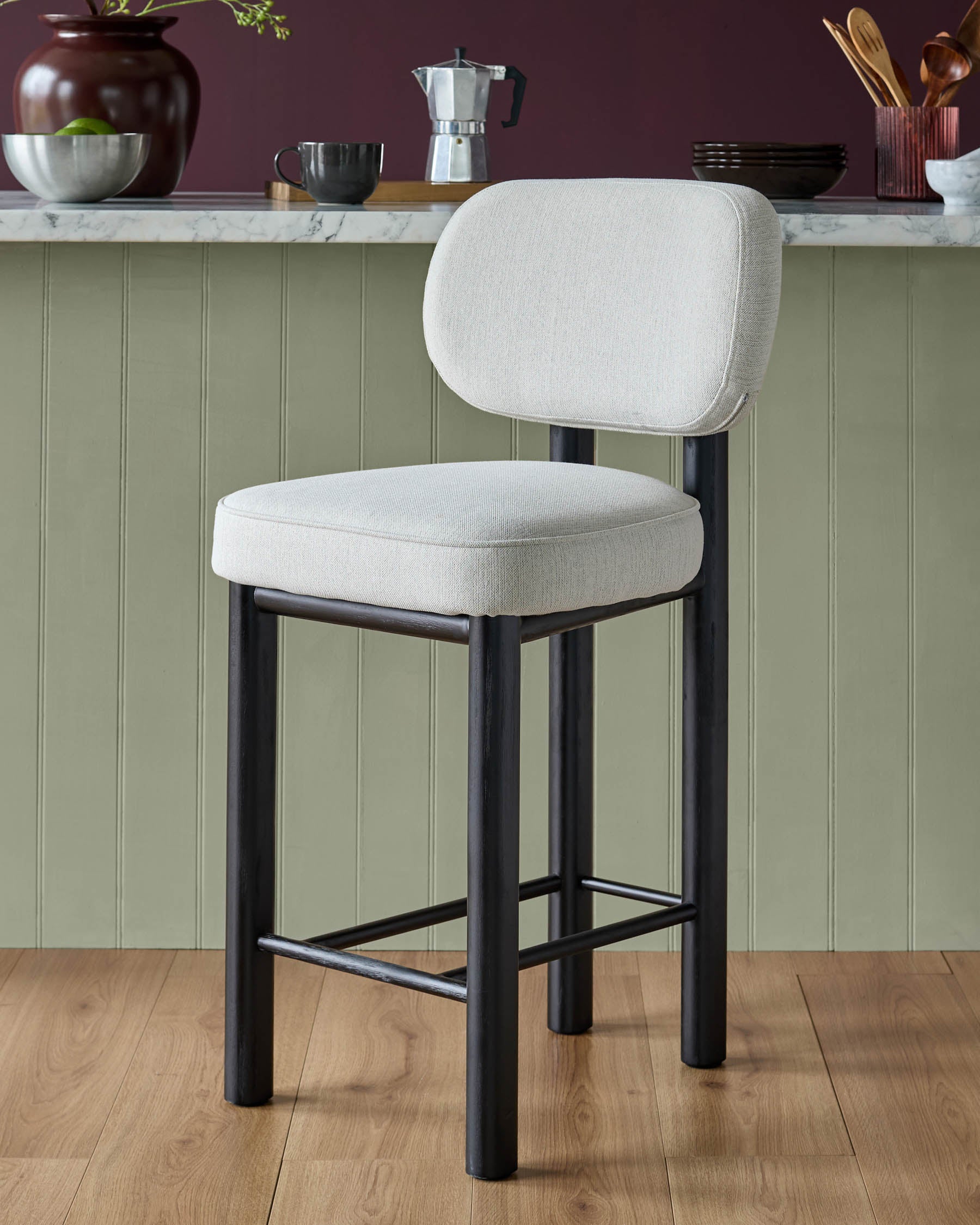 Henley bar stool with ivory fabric seat and backrest, black wooden frame and footrest on wooden flooring.