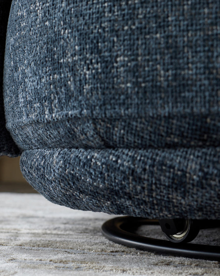 Close-up of a stylish blue fabric armchair with a sleek, black swivel base, resting on a neutral-toned rug.