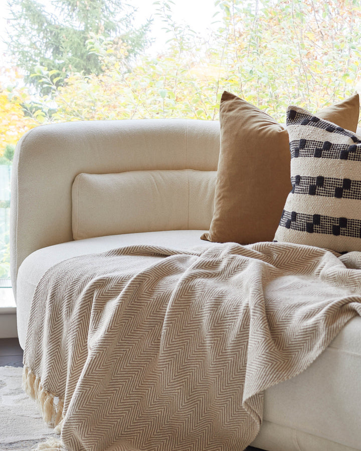 A stylish off-white sofa with tan cushions and a patterned throw, creating a cosy and inviting living space.