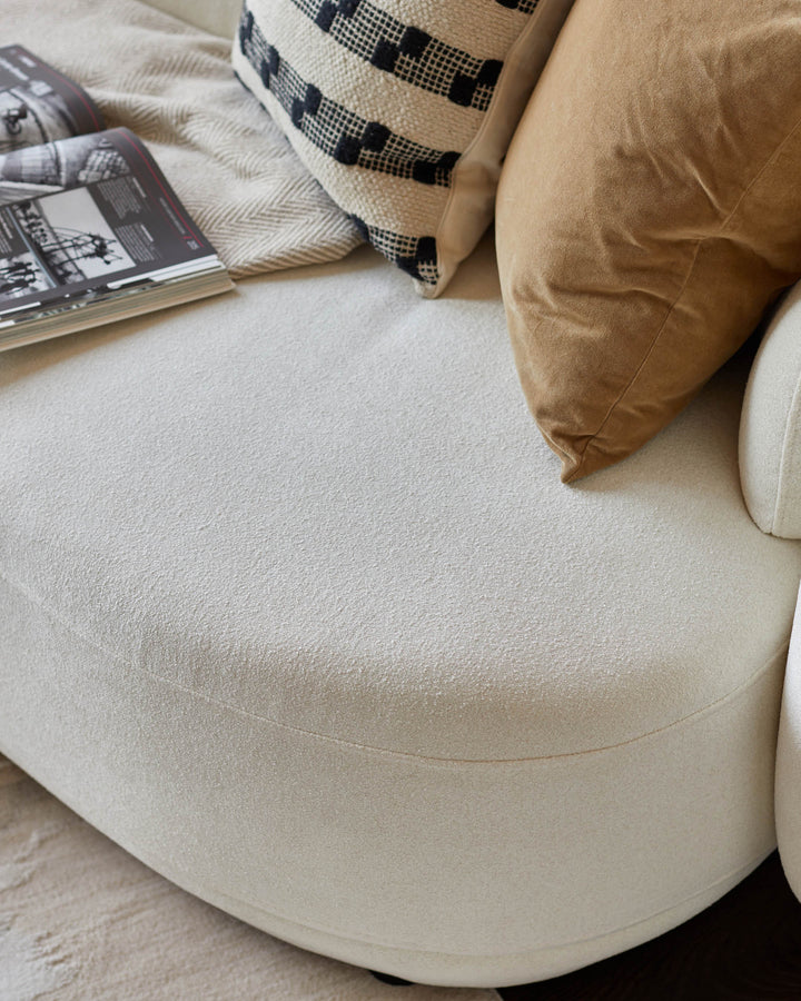 Close-up of a stylish cream-coloured sofa with patterned cushions and a magazine, showcasing its texture and design.