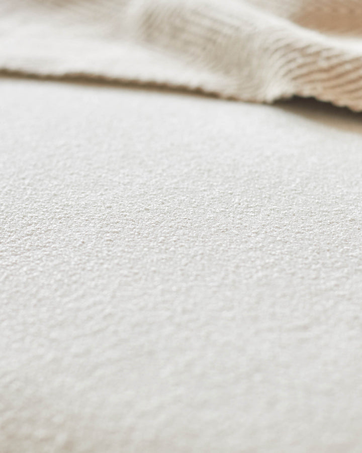 Close-up of neutral textured fabric, possibly upholstery on furniture like a sofa or armchair. Focus on texture and light tones.
